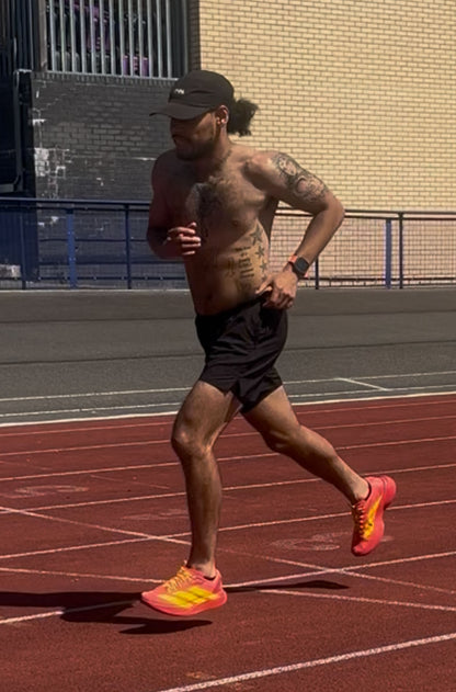 Man running on a track wearing black shorts and bright orange shoes.