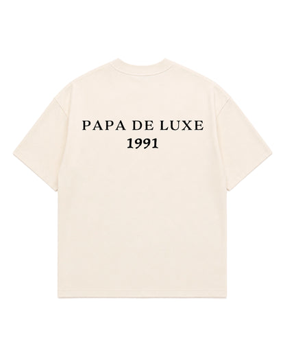 An off-white short-sleeve t-shirt with 'PAPA DE LUXE 1991' printed in black serif text across the chest, displayed on a solid white background.