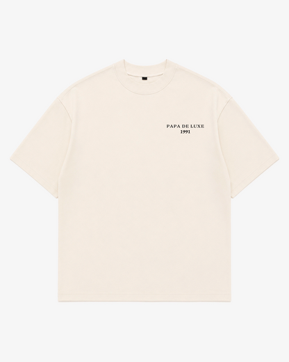 An off-white short-sleeve crewneck t-shirt with 'PAPA DE LUXE 1991' printed in black on the left chest, displayed flat against a light gray background.