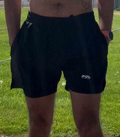 Person wearing black shorts with a visible brand logo on a grassy field.